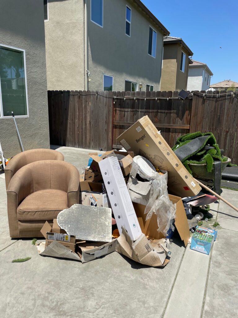 Backyard junk pile with armchairs, boxes and artificial turf before removal