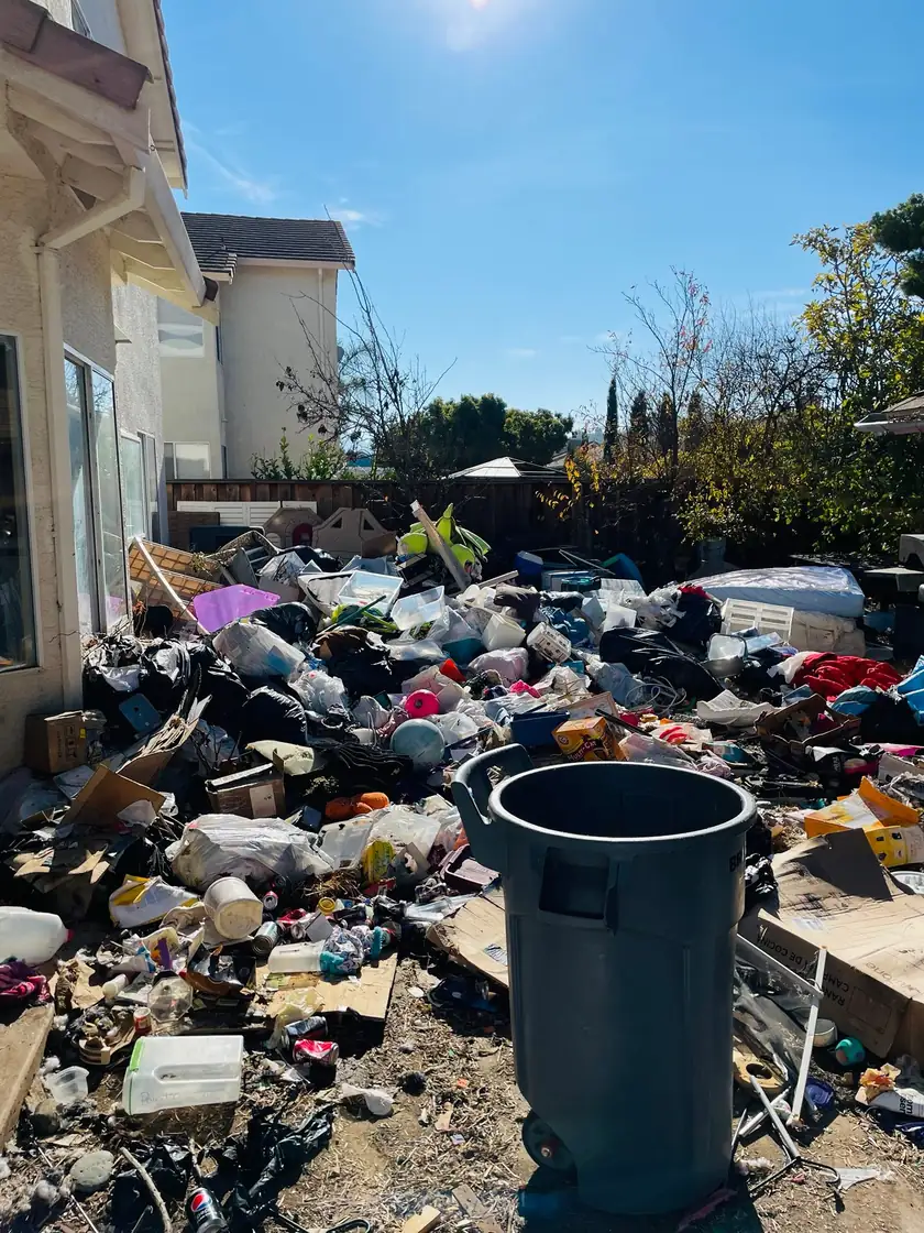 Backyard buried in trash and household items before a hoarder cleanout