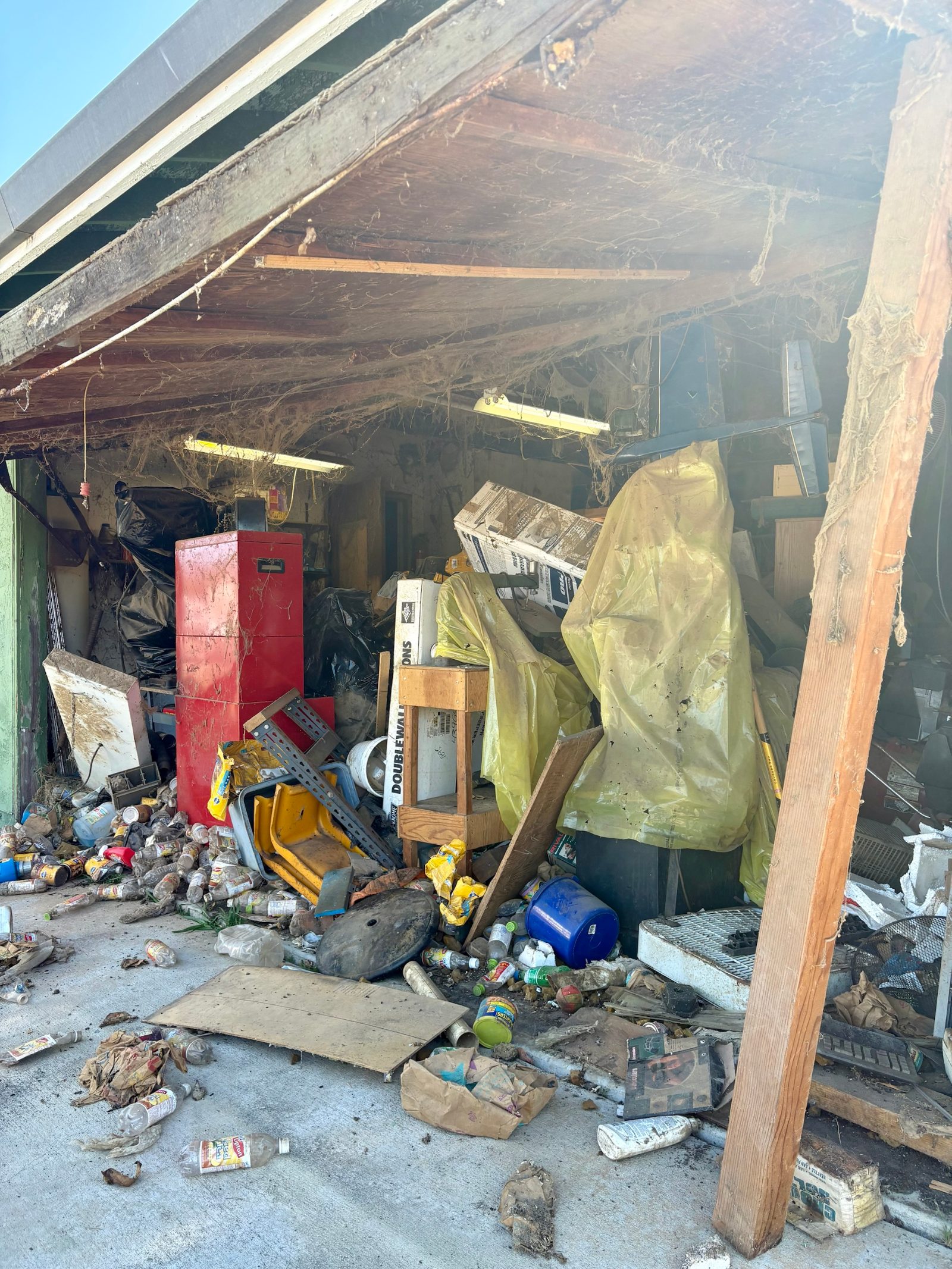 Hoarder garage in Watsonville, CA before cleanout, packed with boxes, a red cabinet and bottles