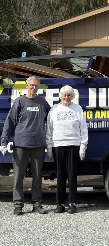 Two happy customers standing in front of the loaded Junk Gone trailer