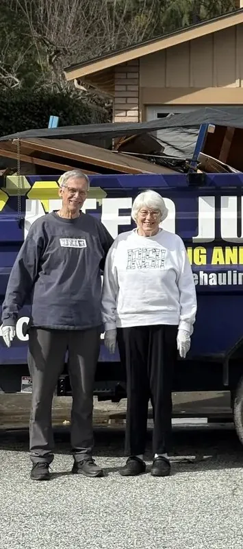 Two happy customers standing in front of the loaded Junk Gone trailer