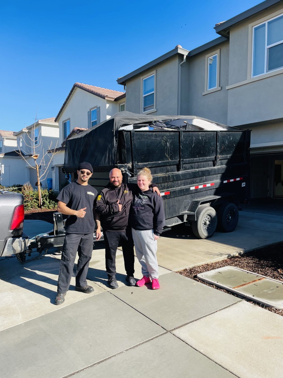 Happy customers giving a thumbs up with the Junk Gone crew in front of the dump trailer