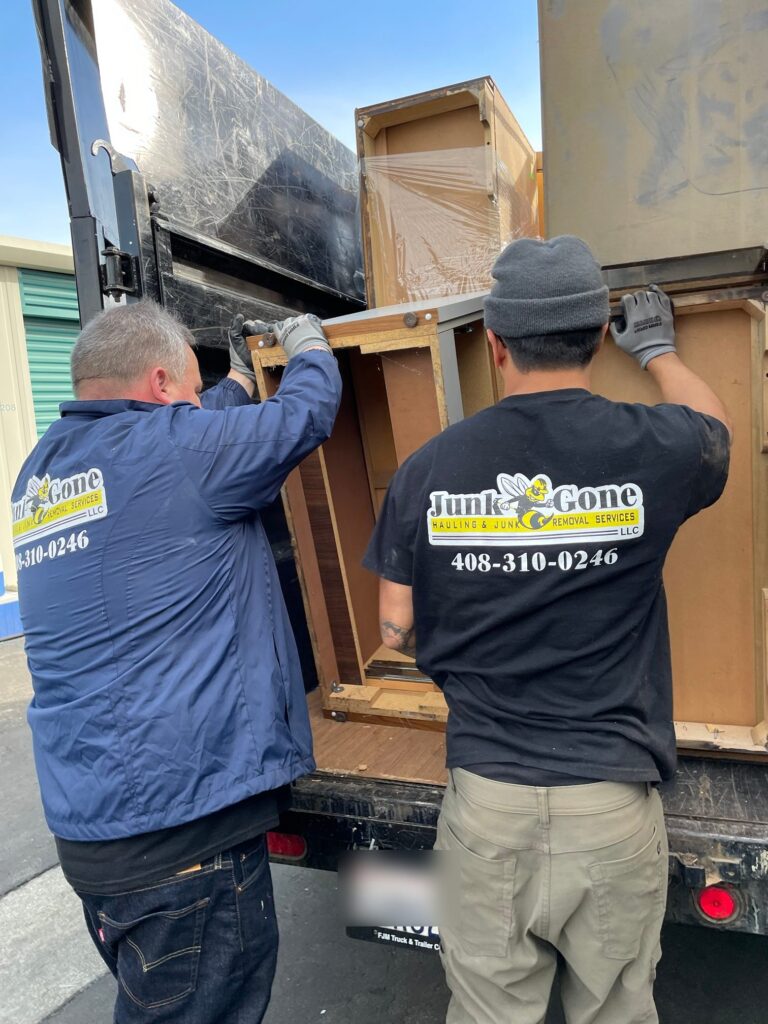 Two Junk Gone crew members lifting a cabinet into the dump trailer