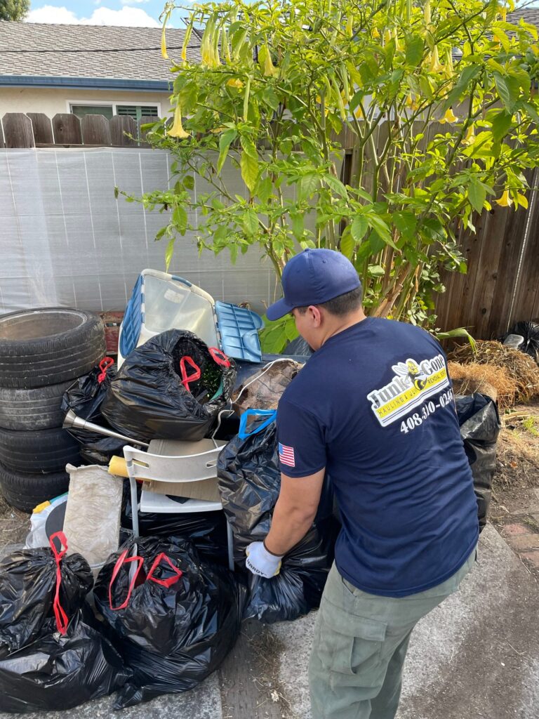 Junk Gone crew member clearing bags, bins and old tires from a backyard