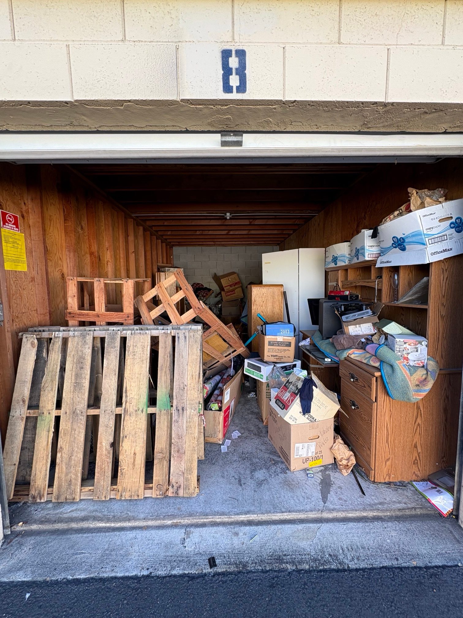 Storage unit before cleanout: pallets, desk, fridge and boxes packed inside