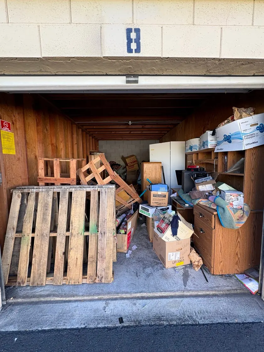 Storage unit before cleanout: pallets, desk, fridge and boxes packed inside